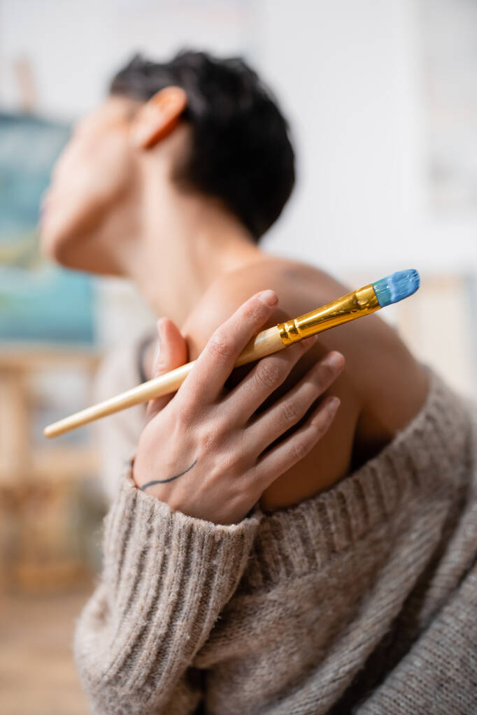 肩に触れるセーターとワークショップで絵筆を保持中のアーティスト  - 写真・画像
