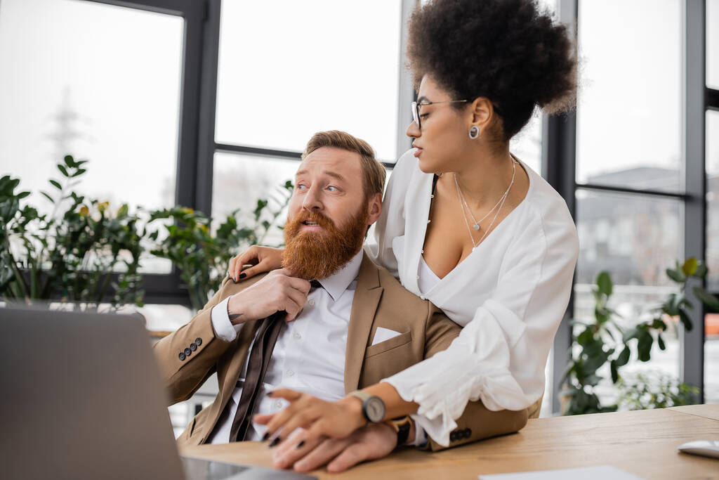 seductive african american woman using laptop near bearded businessman pulling tie in office  - Photo, Image