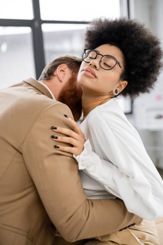 bearded businessman kissing neck of brunette african american woman in glasses  - Zdjęcie, obraz
