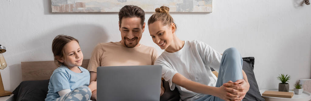 cheerful parents and happy kid watching movie on laptop in bedroom, banner  - Foto, Bild
