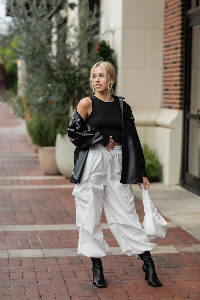 comprimento total da jovem mulher em jaqueta de camisa de couro e calças de carga posando com bolsa na rua em Miami  - Foto, Imagem