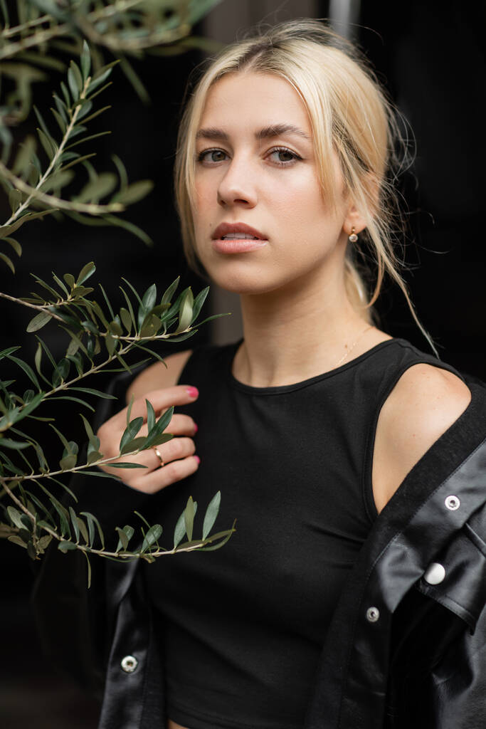 портрет блондинки в кожаной куртке, стоящей рядом с растением  - Фото, изображение