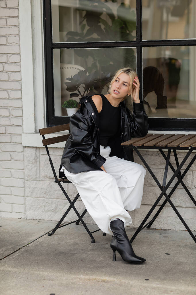 Deri ceketli ve kargo pantolonlu bir kadın Miami 'de açık bir kafede oturuyor.  - Fotoğraf, Görsel