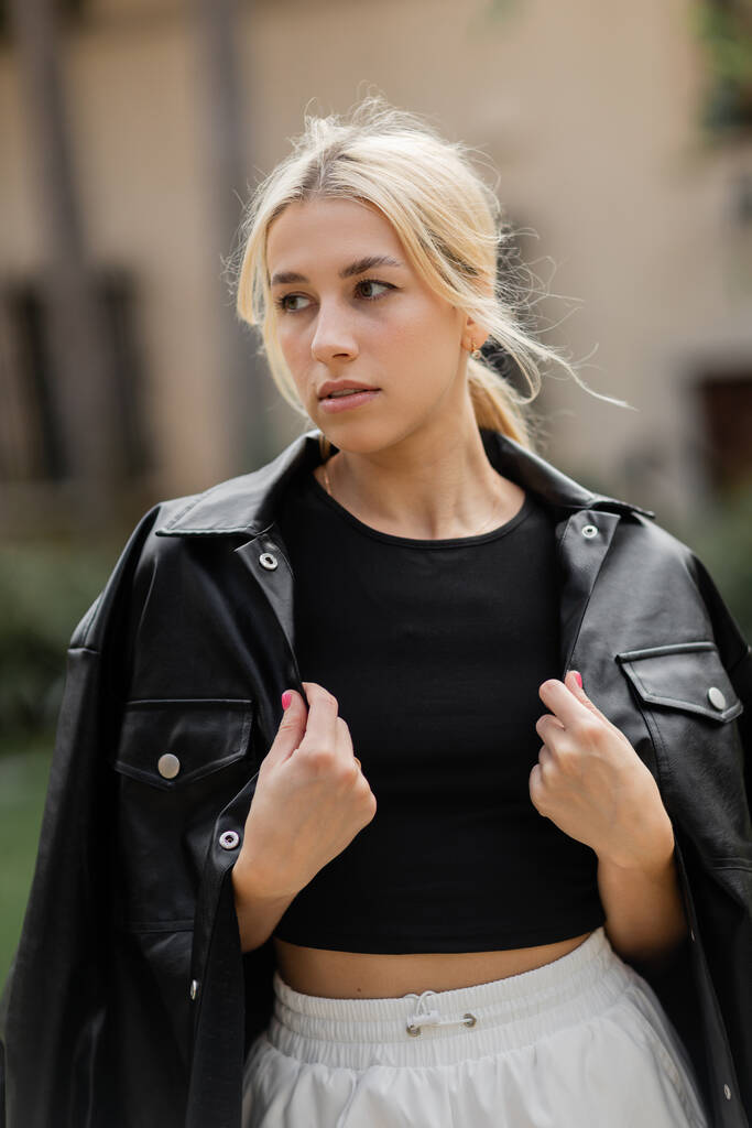 portret van blonde jonge vrouw in zwart shirt jas kijken weg buiten  - Foto, afbeelding