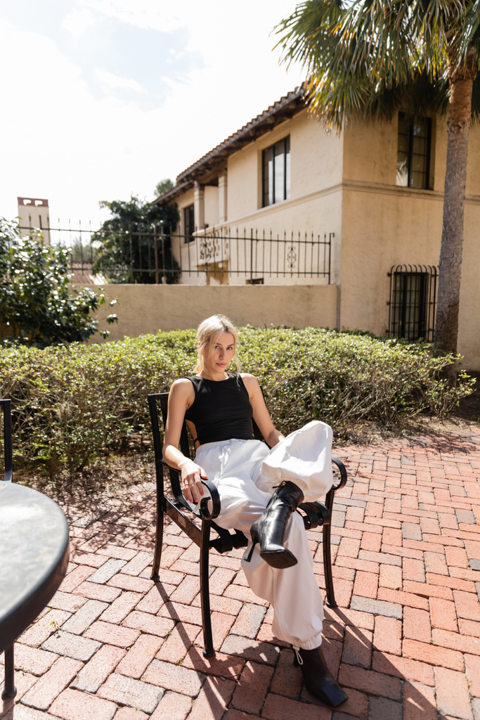 Повна довжина молодої жінки в модному одязі сидить на подвір "ї біля сучасного будинку в Маямі.  - Фото, зображення