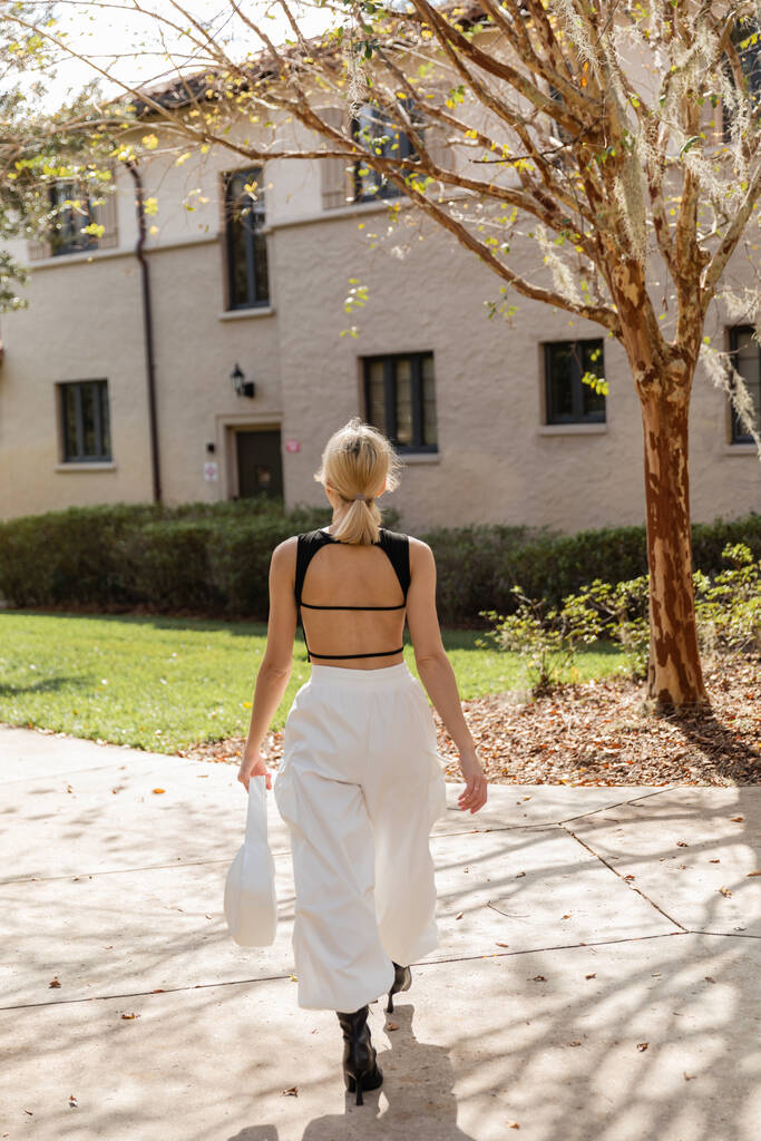 Rückansicht einer blonden Frau mit Handtasche, die in der Nähe ihres Hauses in Miami spaziert  - Foto, Bild
