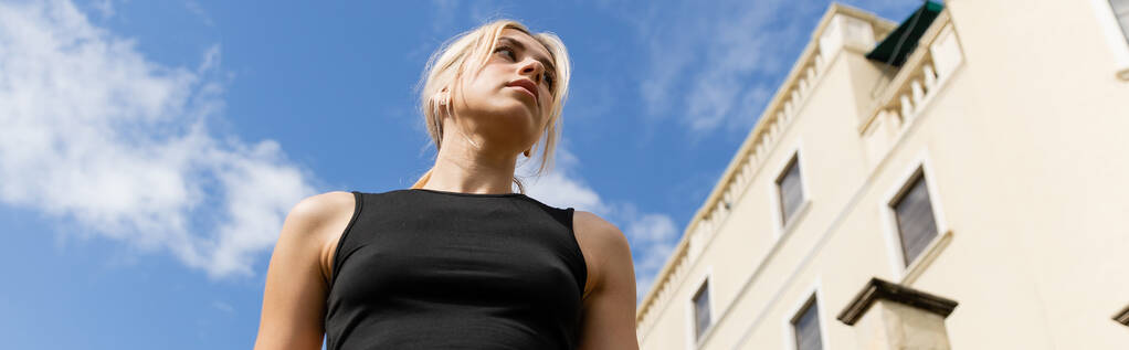 low angle view of blonde woman in tank top standing near building in Miami, banner  - Photo, Image