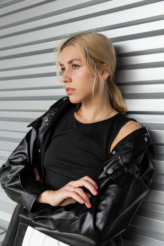 Молода блондинка в шкіряній куртці стоїть біля дверей гаража в Маямі.  - Фото, зображення