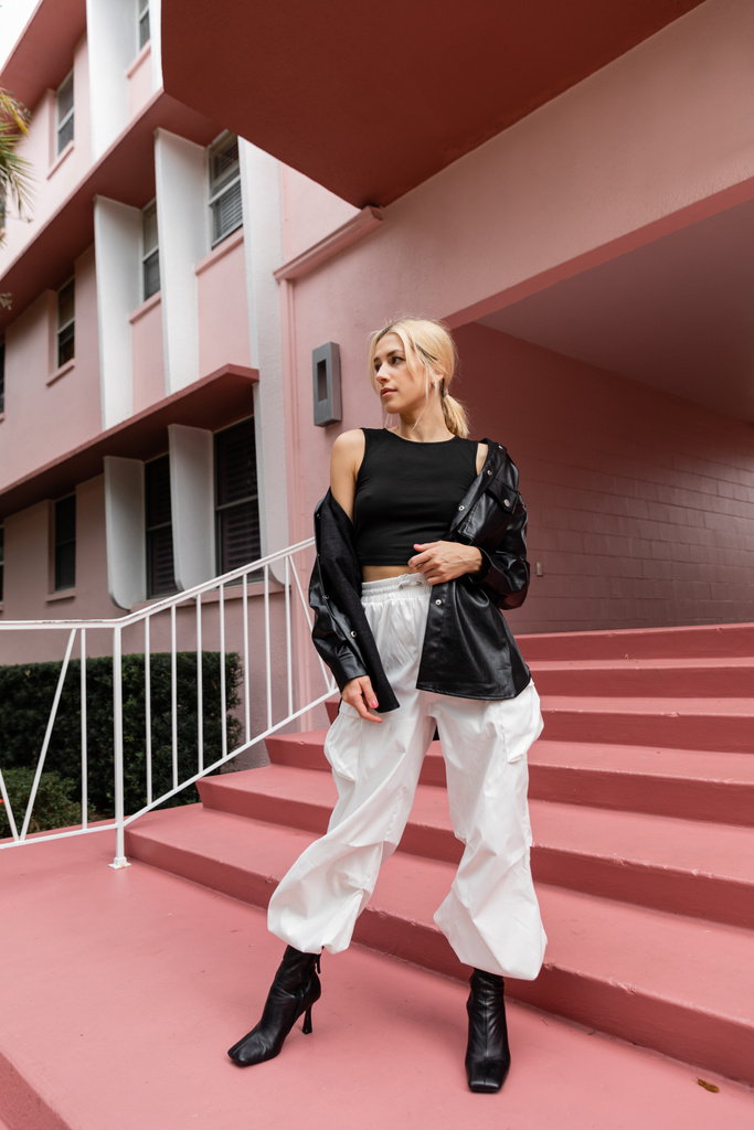 pleine longueur de jeune femme blonde en débardeur noir et pantalon cargo debout sur des escaliers roses à Miami  - Photo, image