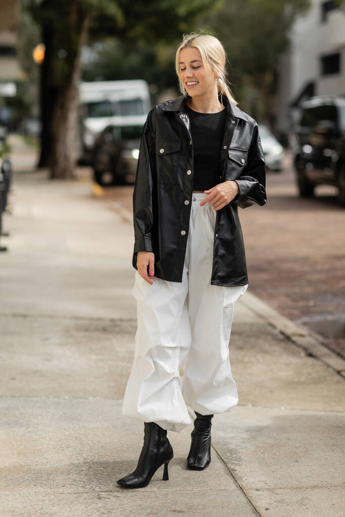 plná délka veselá žena v kožené košili bunda a nákladní kalhoty chůze na městské ulici v Miami  - Fotografie, Obrázek