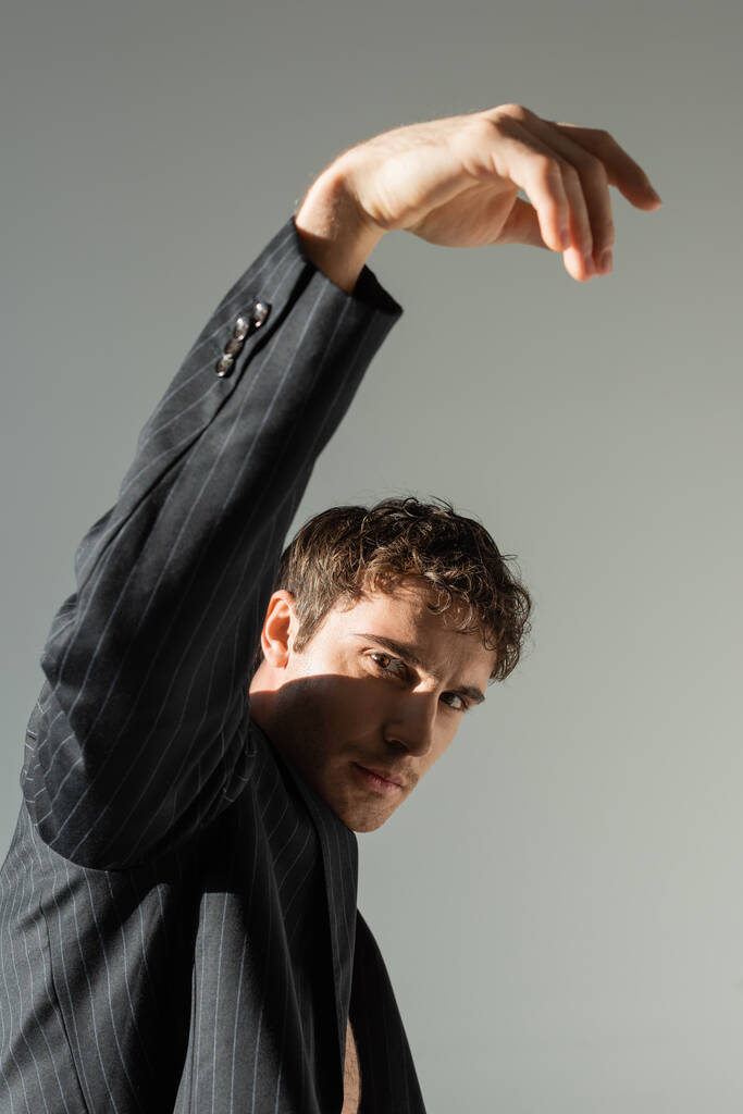 брюнетка чоловік в чорному і смугастому блістері позує з піднятою рукою, дивлячись на камеру ізольовано на сірому
 - Фото, зображення