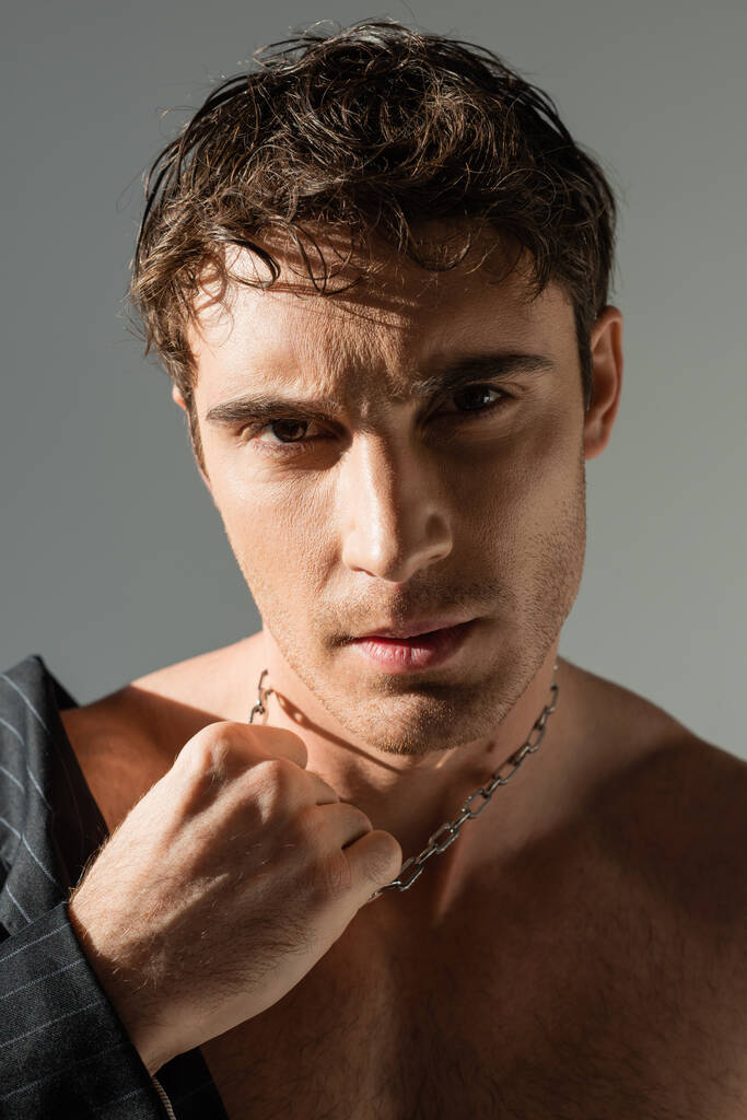 portrait of sexy brunette man touching silver necklace and looking at camera isolated on grey - Fotoğraf, Görsel