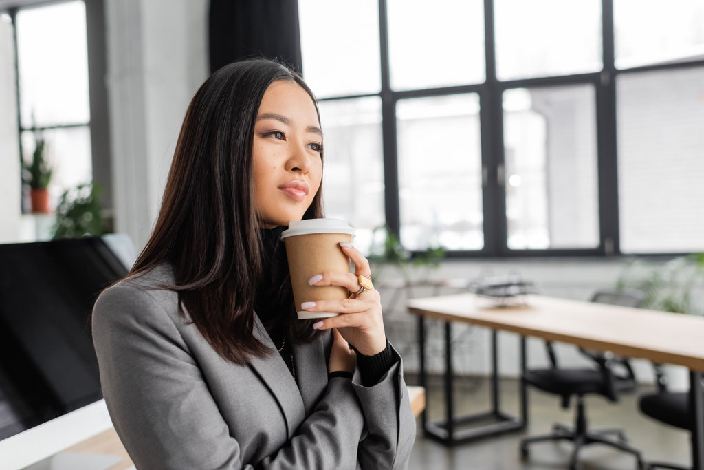 Dreamy asian interior designer holding coffee to go and thinking in office  - Foto, immagini