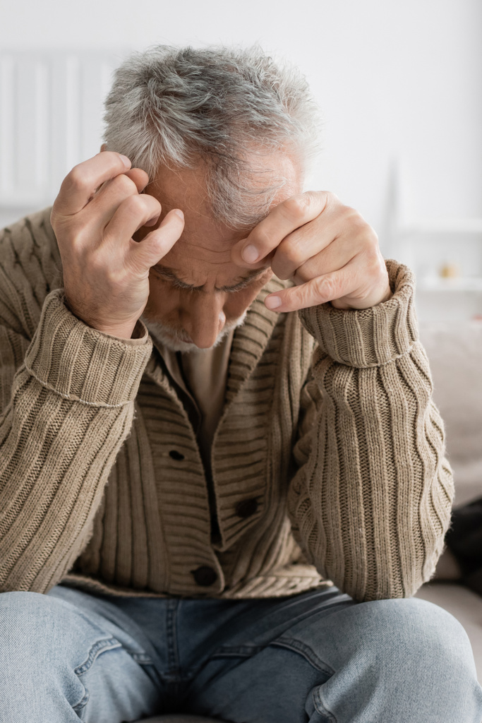 aged man with parkinsonian syndrome and trembling hands sitting with bowed head at home - Foto, immagini