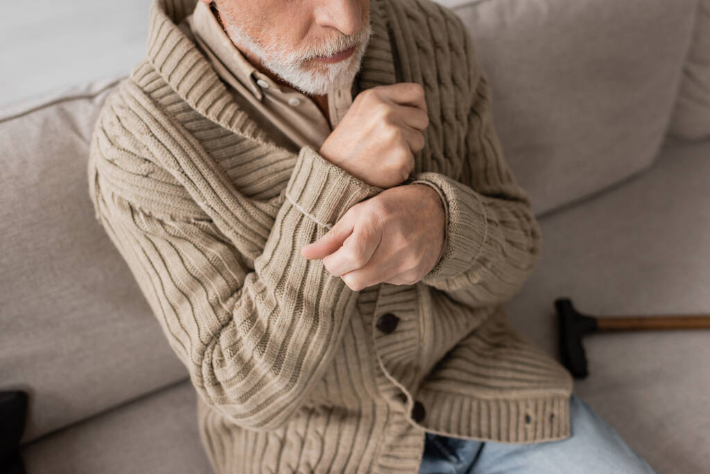 cropped view of senior man in knitted cardigan suffering from parkinsonism and tremor in hands while sitting at home - Foto, Imagem