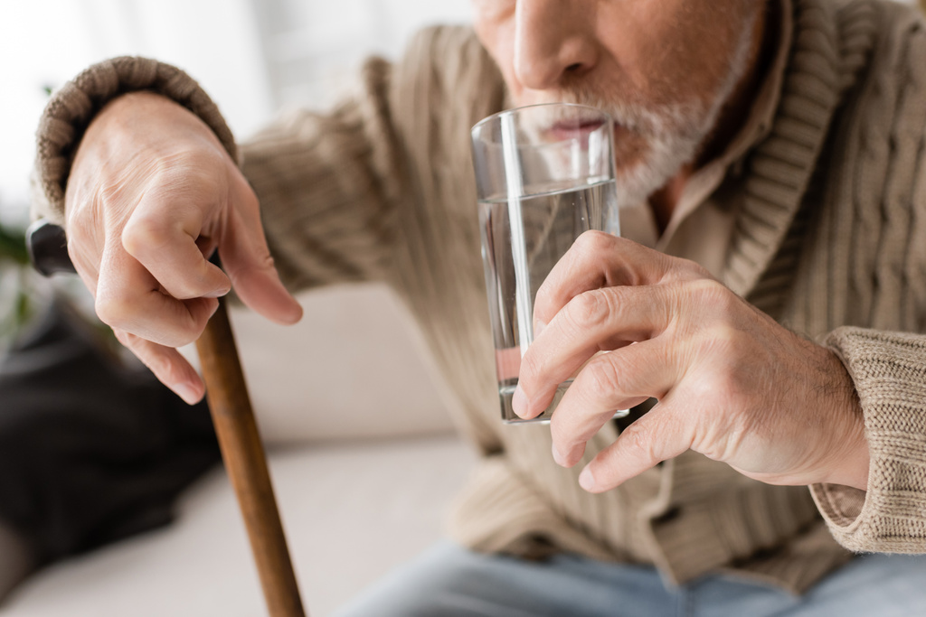 partial view of senior man with parkinsonism and tremor in hands drinking water at home - Foto, Imagem