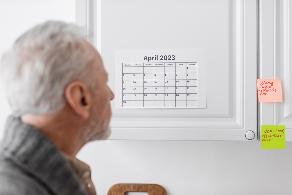 blurred senior man suffering from memory loss and looking at calendar and sticky notes in kitchen - Photo, Image