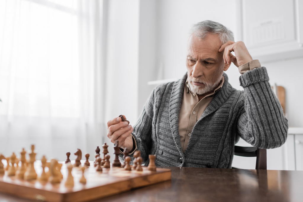 grey haired man with alzheimer disease holding chess figure and thinking at home - Photo, Image