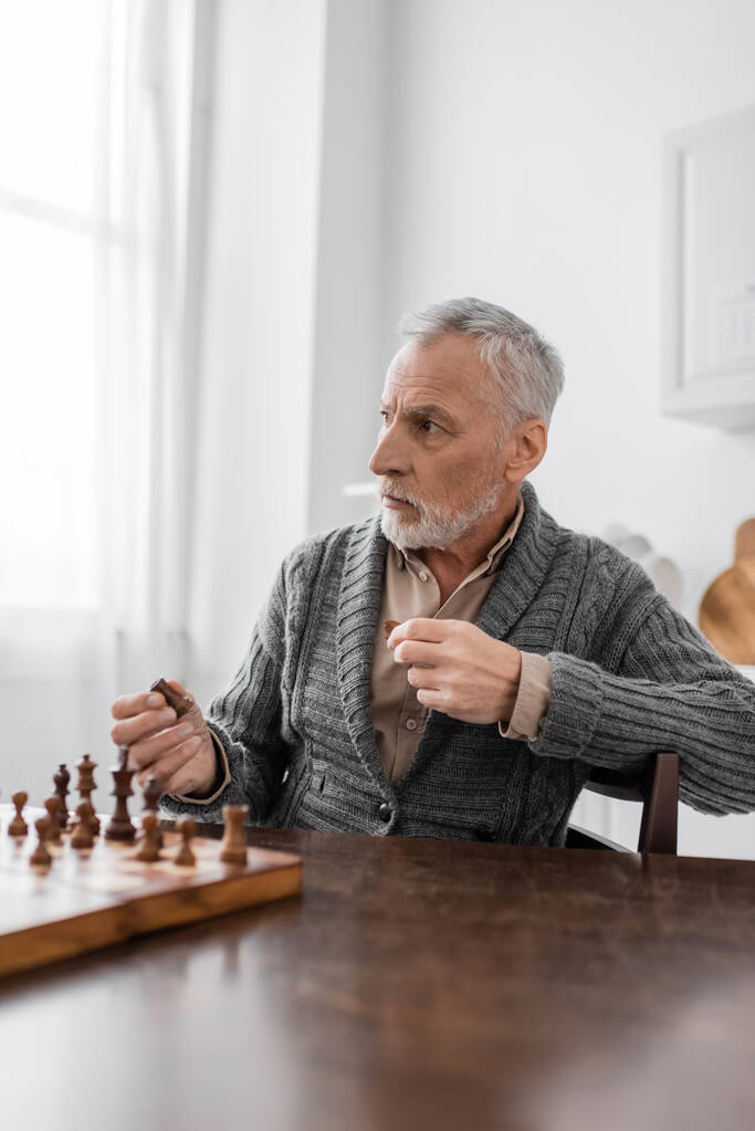 aged man with alzheimer disease holding chess figure and looking away - Foto, immagini