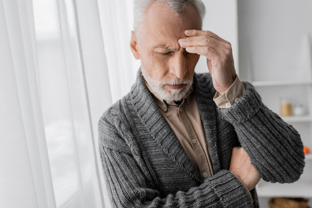 depressed senior man with alzheimer syndrome standing with closed eyes and touching forehead at home - Fotó, kép