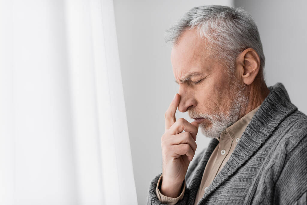 вид збоку депресивного старшого чоловіка з синдромом Альцгеймера, який торкається обличчя, стоячи вдома
 - Фото, зображення