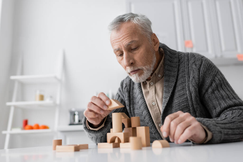 bearded senior man suffering from alzheimer disease and playing building blocks game on table at home - Foto, Bild