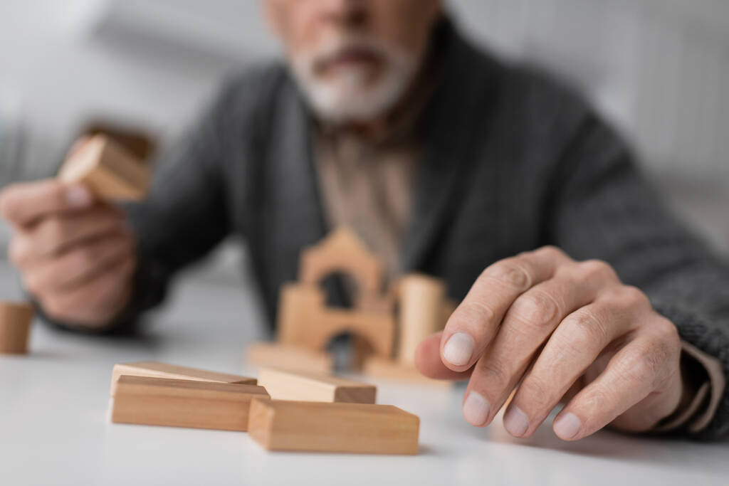 partial view of aged man sick on alzheimer syndrome playing building blocks game on blurred background - Fotó, kép