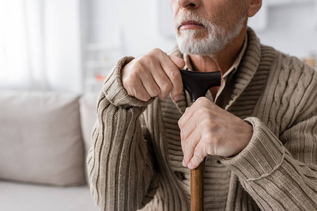 partial view of senior bearded man with parkinson syndrome sitting with walking cane at home - Valokuva, kuva