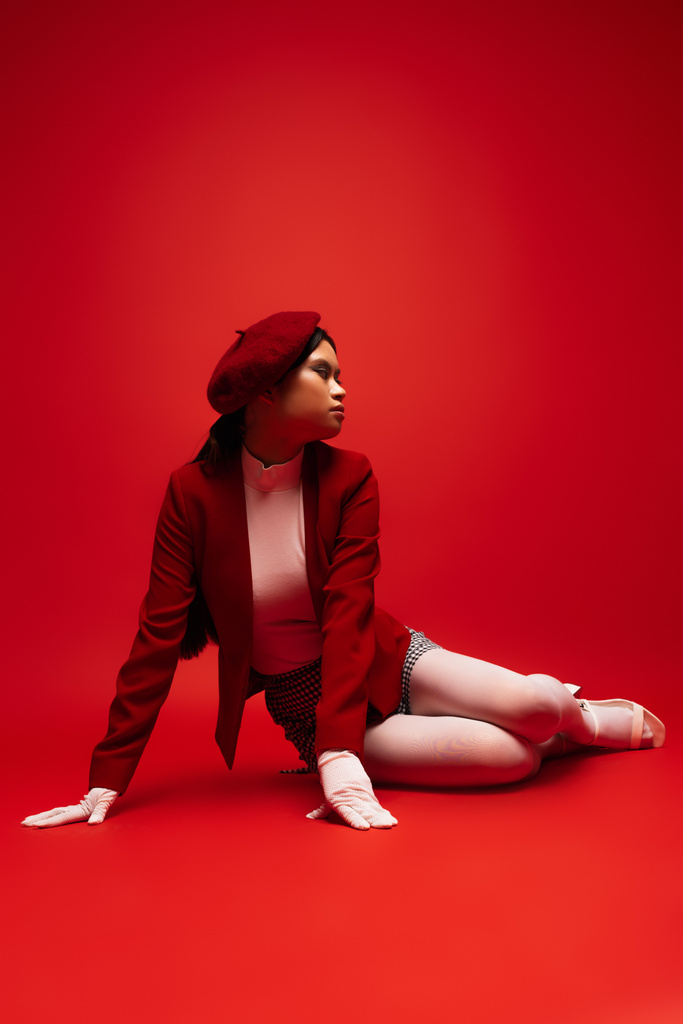 Pretty young asian model in stylish outfit sitting on red background  - Zdjęcie, obraz