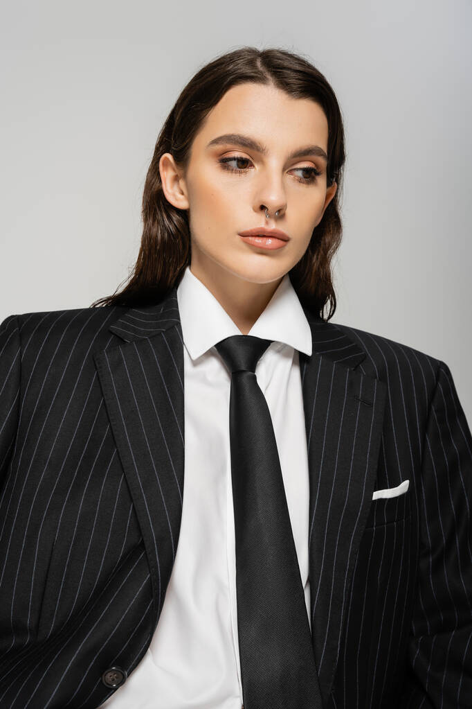 brunette woman in white shirt and black striped jacket with tie isolated on grey - Zdjęcie, obraz