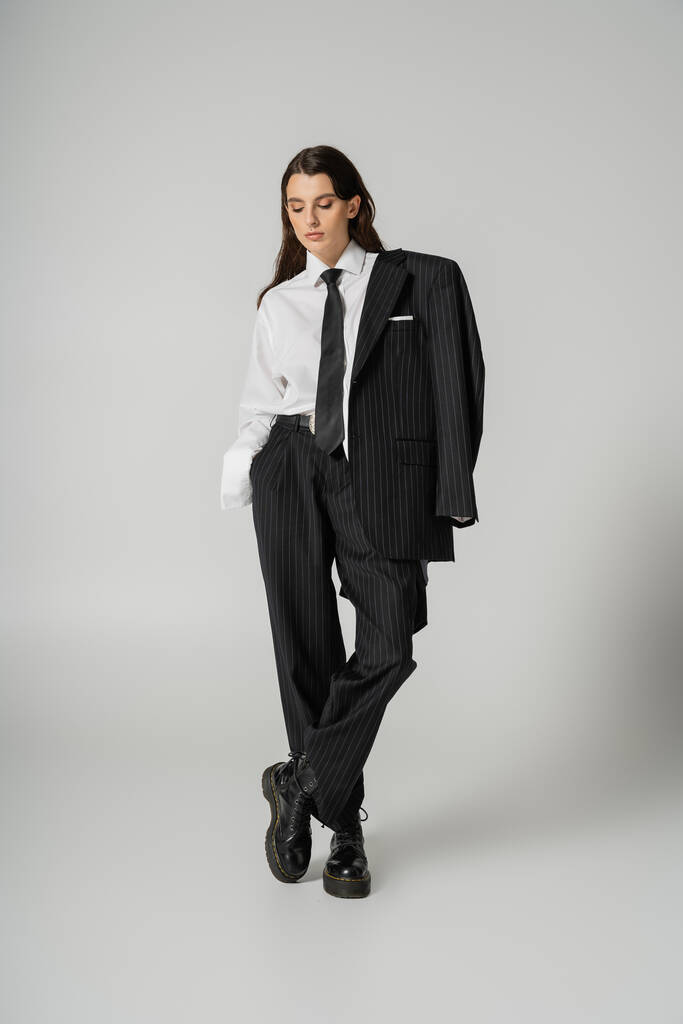 full length of young woman in elegant formal wear and rough leather boots posing with hand in pocket isolated on grey - Foto, Imagem