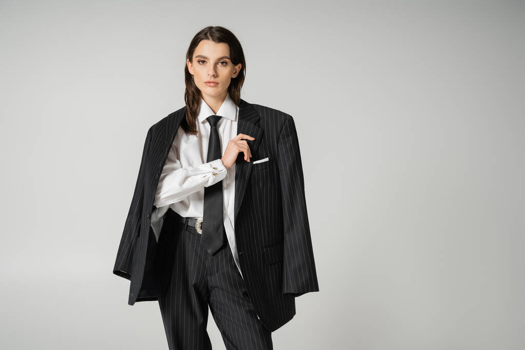 brunette model in white shirt and black trousers with blazer looking at camera isolated on grey - Foto, imagen