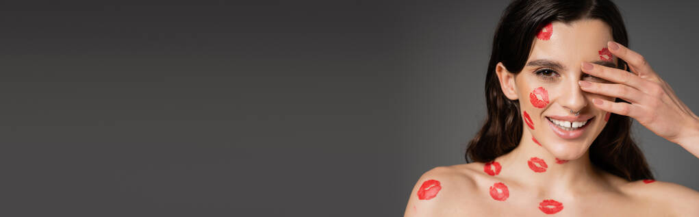 happy shirtless woman with red kiss prints on face and body covering eye with hand isolated on grey, banner - Foto, imagen