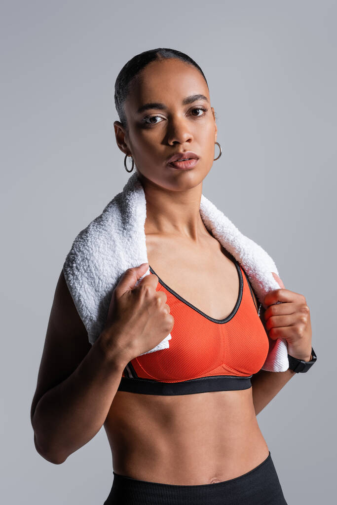 young african american sportswoman in red sports bra standing with towel isolated on grey  - Фото, изображение