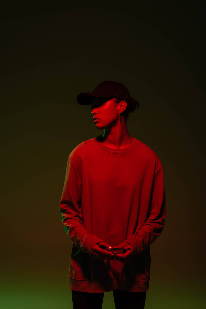 young african american woman in baseball cap and sweatshirt standing on green with red light  - Fotó, kép