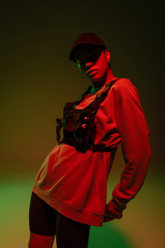 african american woman in baseball cap and sweatshirt standing on green with red light  - 写真・画像