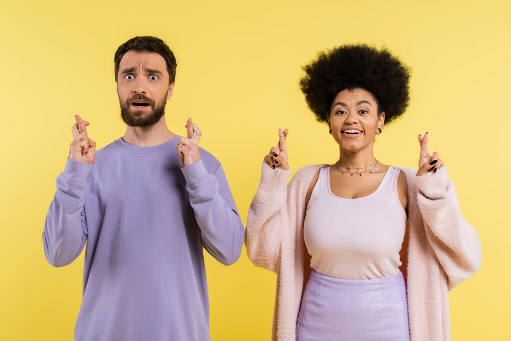 worried bearded man and optimistic african american woman crossing fingers isolated on yellow - Foto, Imagem