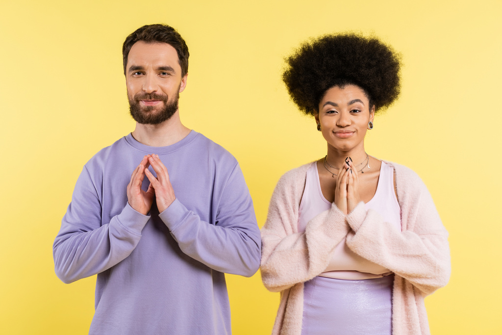 cunning interracial couple smiling at camera and showing please gesture isolated on yellow - Fotoğraf, Görsel