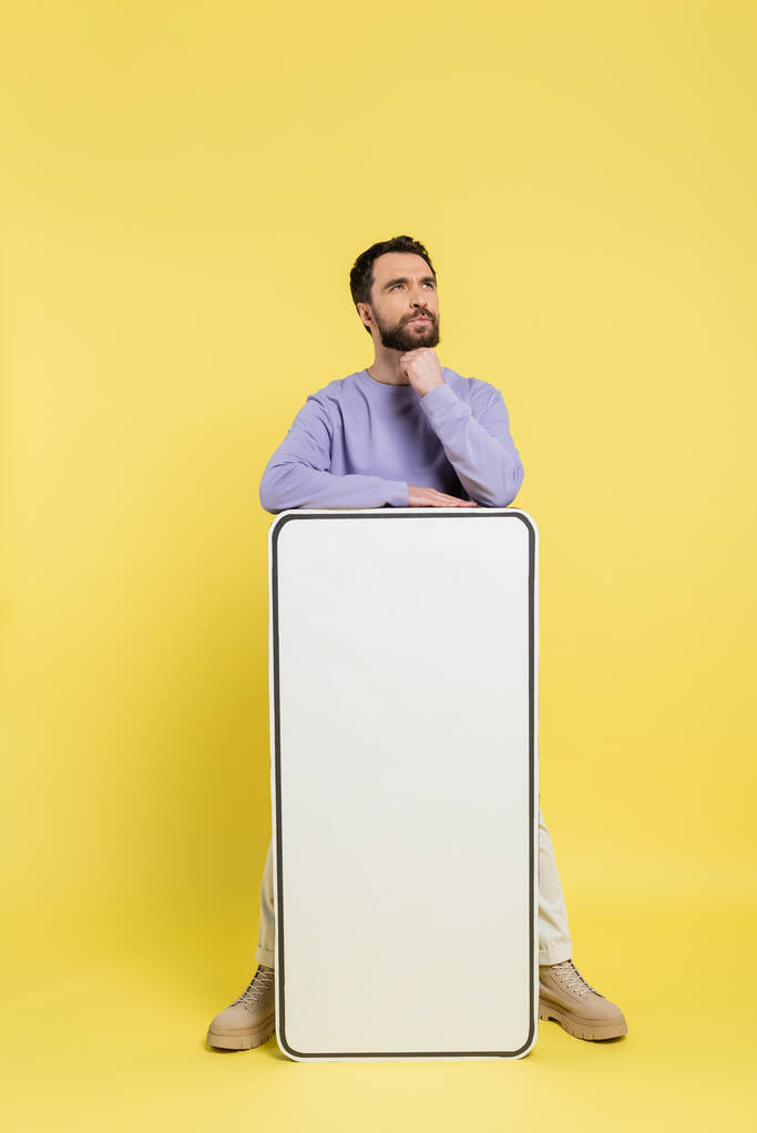 вдумливий бородатий чоловік дивиться далеко від макету білого мобільного телефону на жовтому фоні
 - Фото, зображення