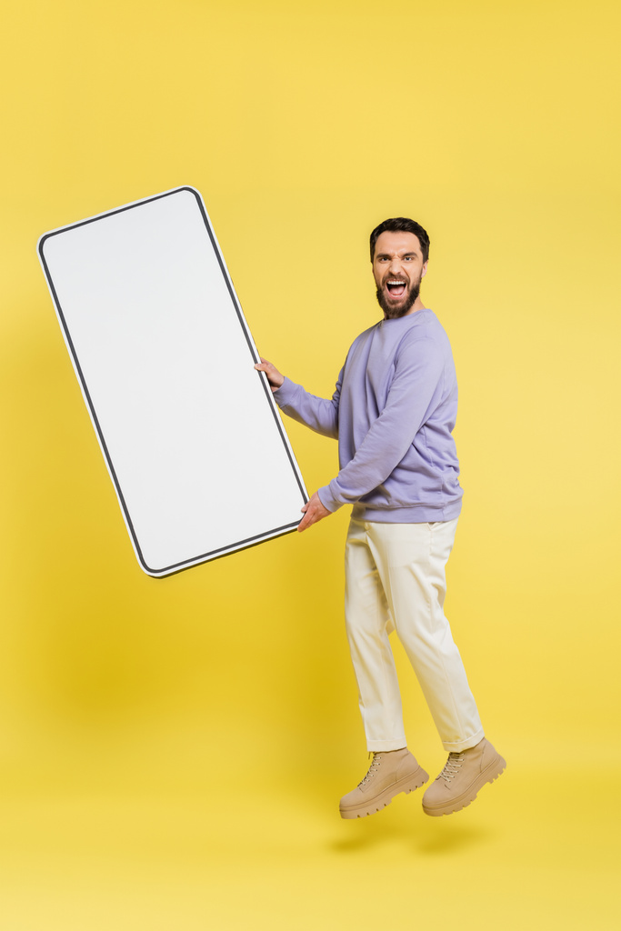 full length of excited bearded man levitating with huge mobile phone template on grey background - Foto, imagen