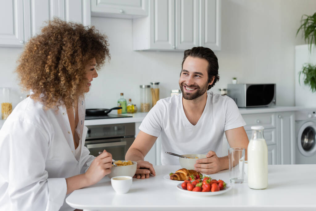 happy bearded man smiling while looking at curly girlfriend during breakfast  - Foto, Imagem