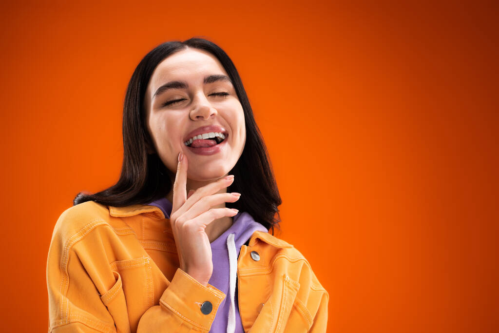 Young brunette woman sticking out tongue isolated on orange - Valokuva, kuva