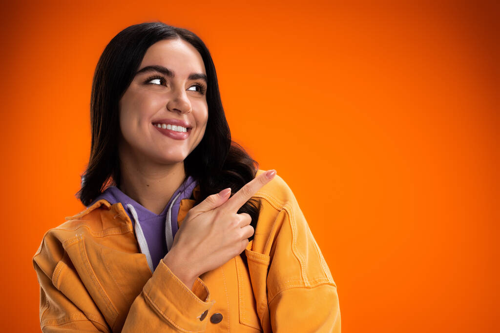 Cheerful brunette woman pointing with finger isolated on orange - Fotó, kép