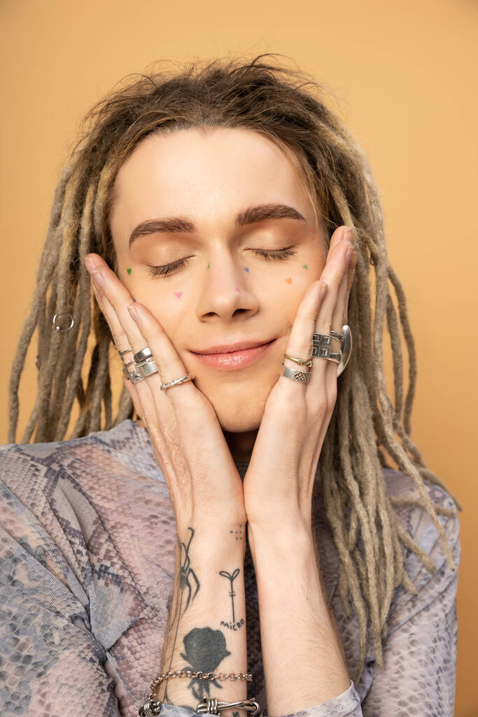 Portrait of pleased tattooed queer person touching face isolated on yellow  - Foto, Imagem