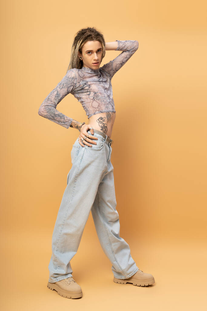 Full length of tattooed nonbinary person looking at camera on yellow background  - Zdjęcie, obraz