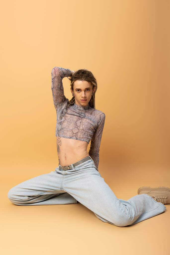 Trendy nonbinary person in crop top posing while sitting on yellow background  - Fotografie, Obrázek