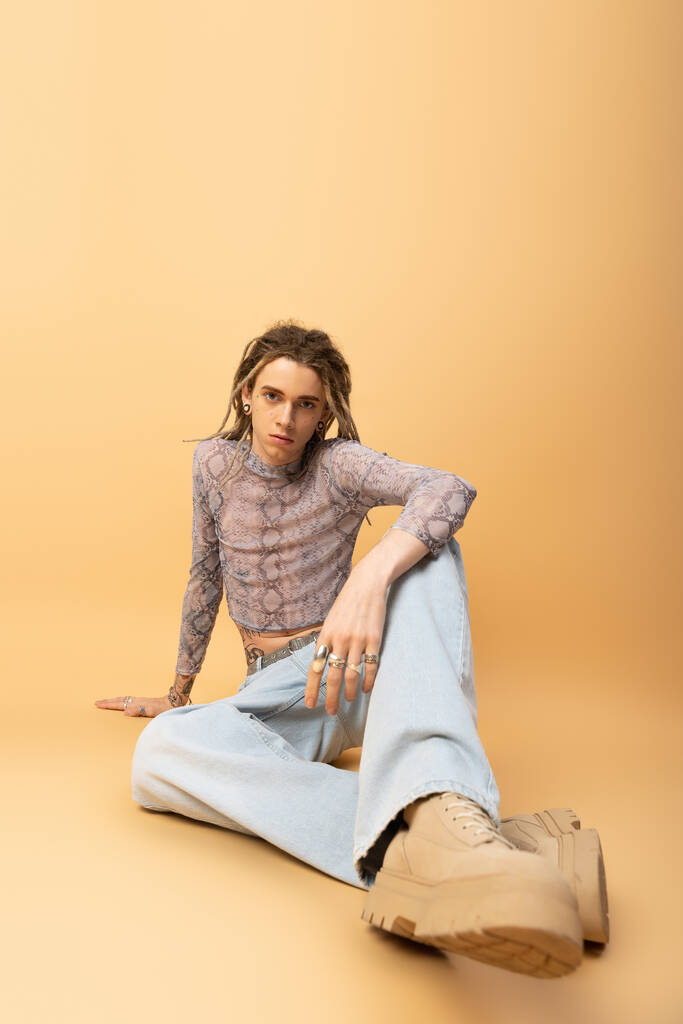 Stylish queer person in jeans and crop top sitting on yellow background  - Φωτογραφία, εικόνα