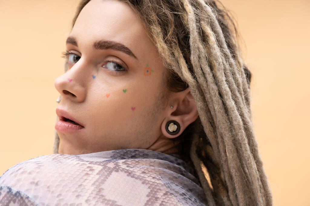 Portrait of young nonbinary person with tattoo and dreadlocks posing isolated on yellow  - Zdjęcie, obraz