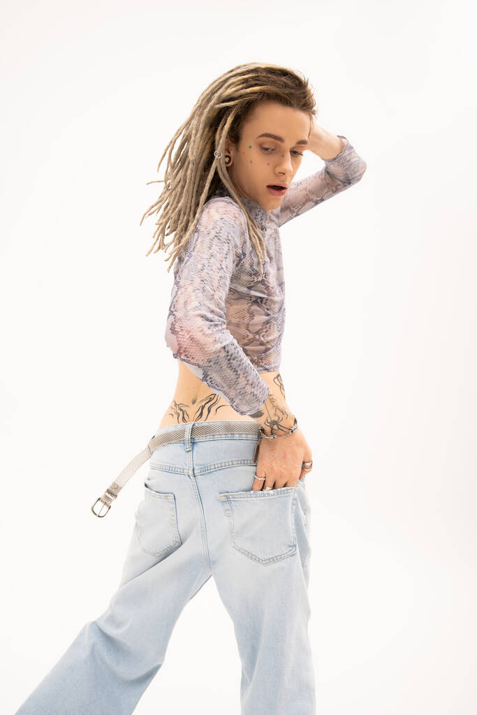 Tattooed queer person in crop top with snakeskin print and jeans posing isolated on white  - Photo, image