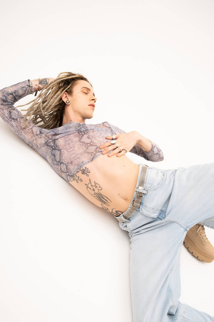 Young tattooed queer person in jeans and crop top posing on white background - Foto, afbeelding